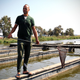 A man stands on a concrete slab between two sections of water. He's holding a fishing net.